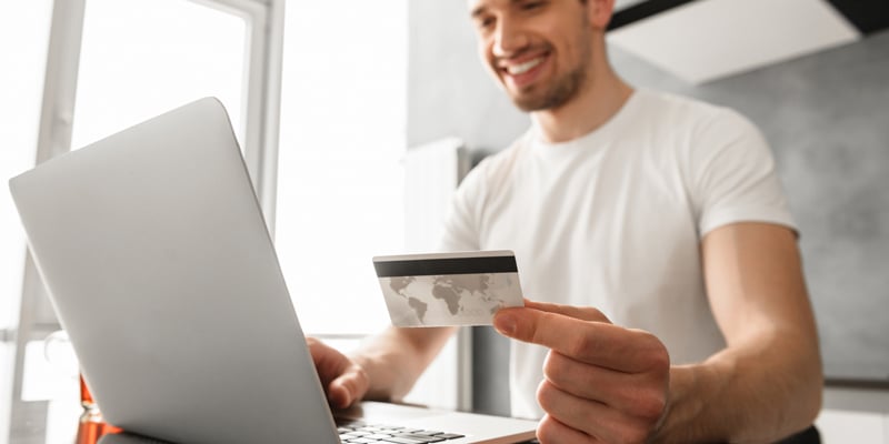Foto de un hombre frente a una laptop sosteniendo una tarjeta de credito.